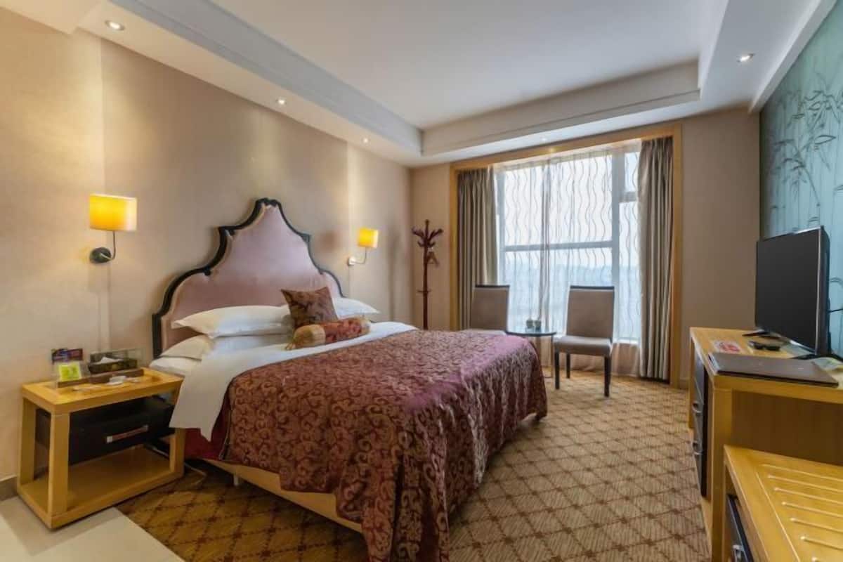 Hotellihuone, jossa on suuri sänky, yöpöydät, työpöytä tuolilla, televisio ja ikkuna, jossa on verhot.