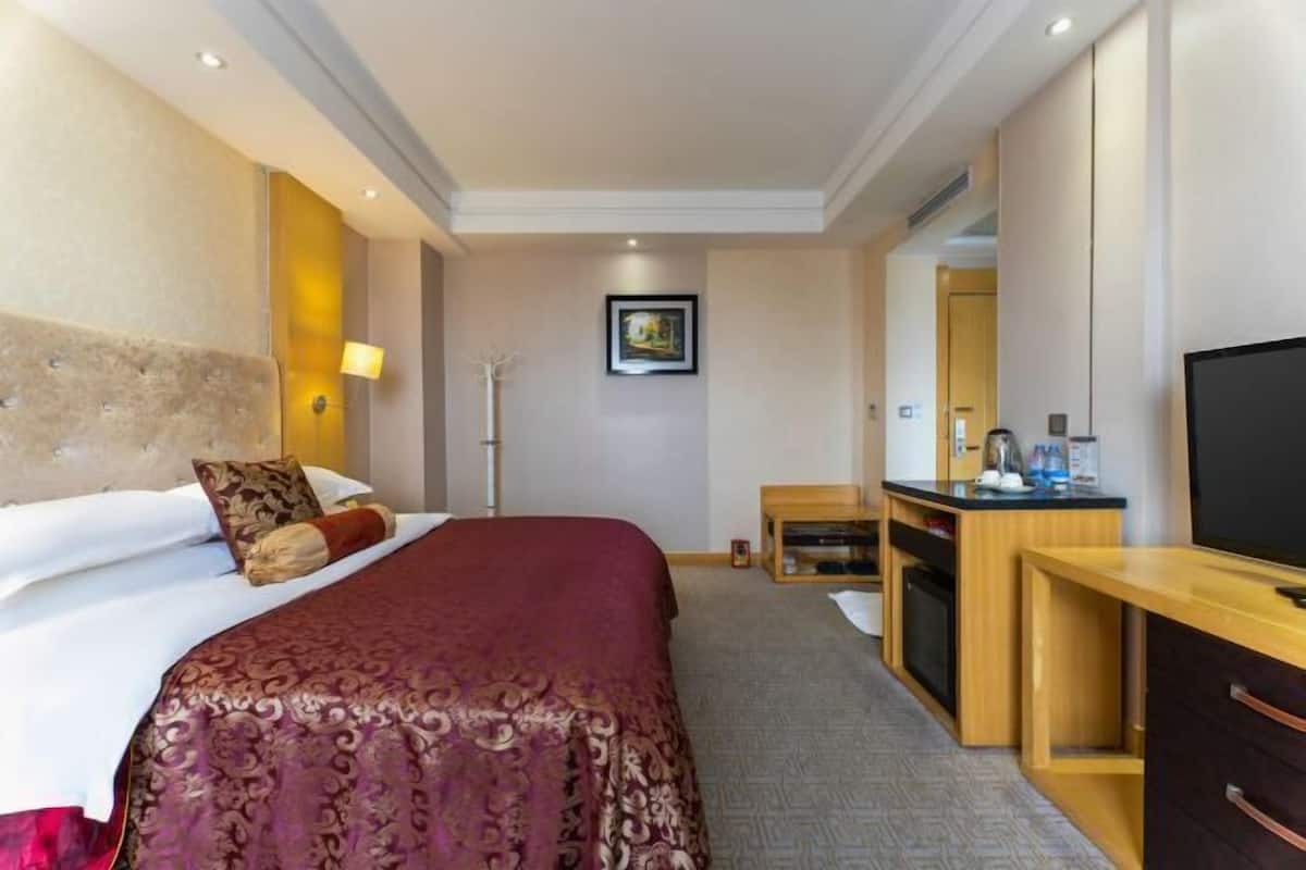 Hotellihuone, jossa on sänky, yöpöytä, televisio ja työpöytä, jossa on peili.