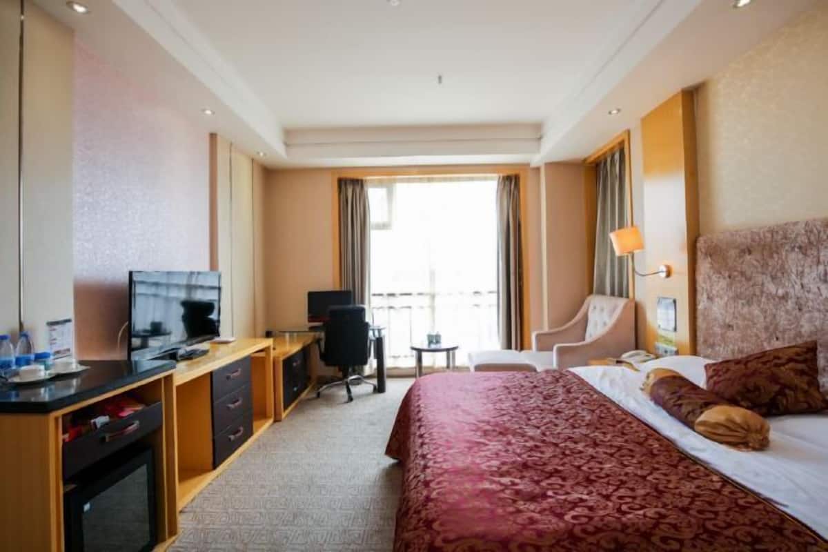 Hotellihuone, jossa on sänky, työpöytä, jossa on televisio, tuoli, pieni pöytä ja näkymä ulos.