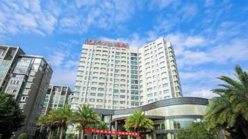 A multi-story hotel with a prominent red sign, surrounded by palm trees and other buildings.