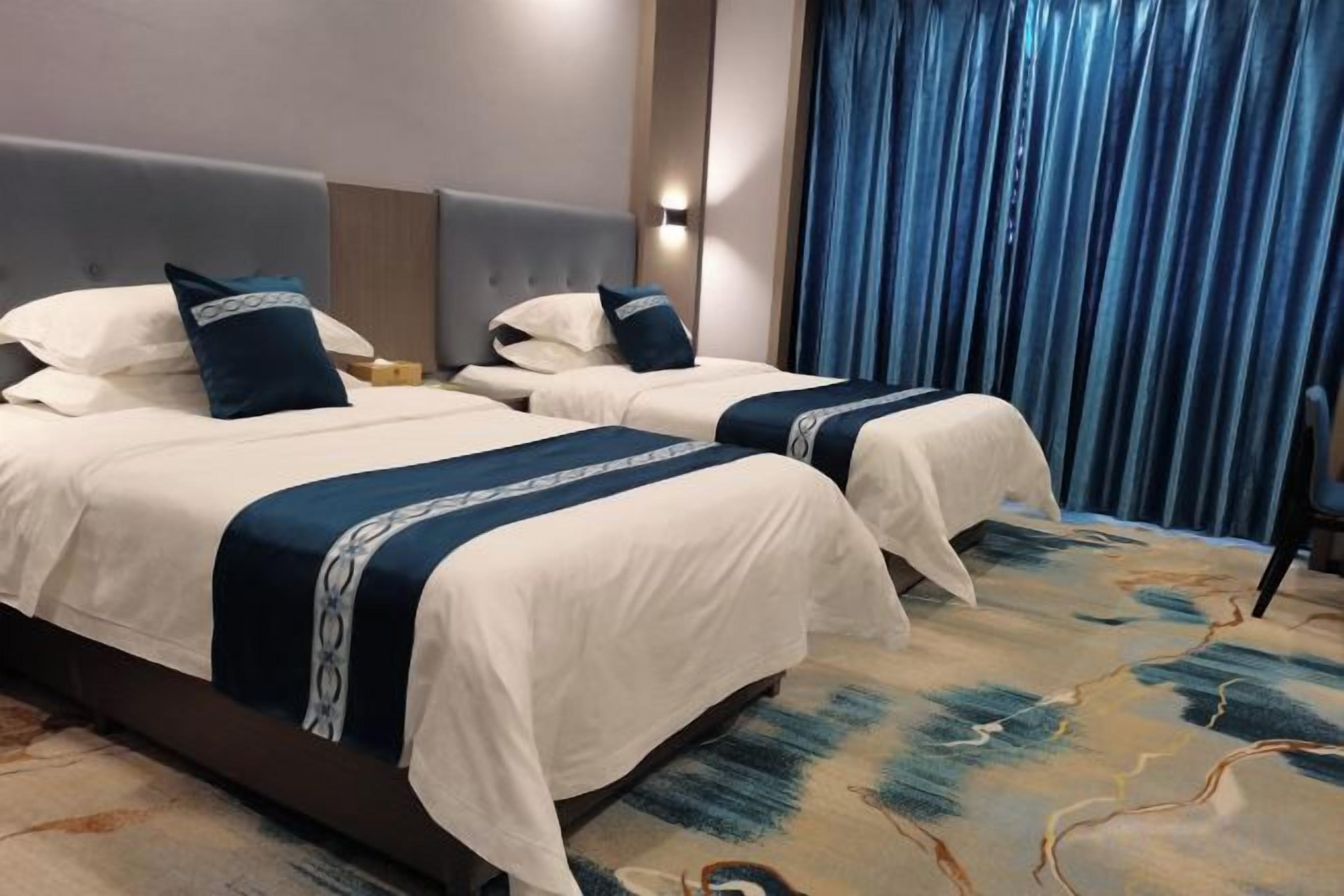 Habitación de hotel con dos camas, cabecero, mesita de noche y cortina azul.