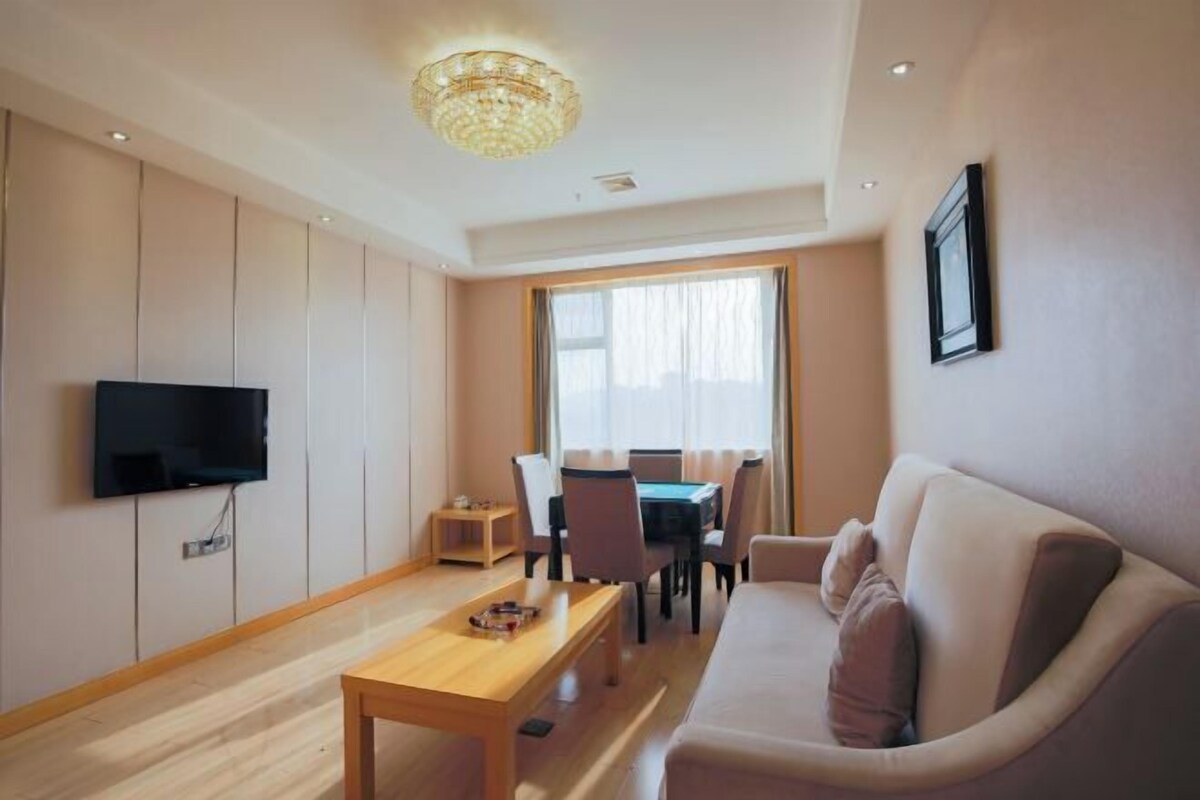 A modern living room with a flat-screen TV, a wooden coffee table, a beige sofa, and a dining area with a table and chairs.