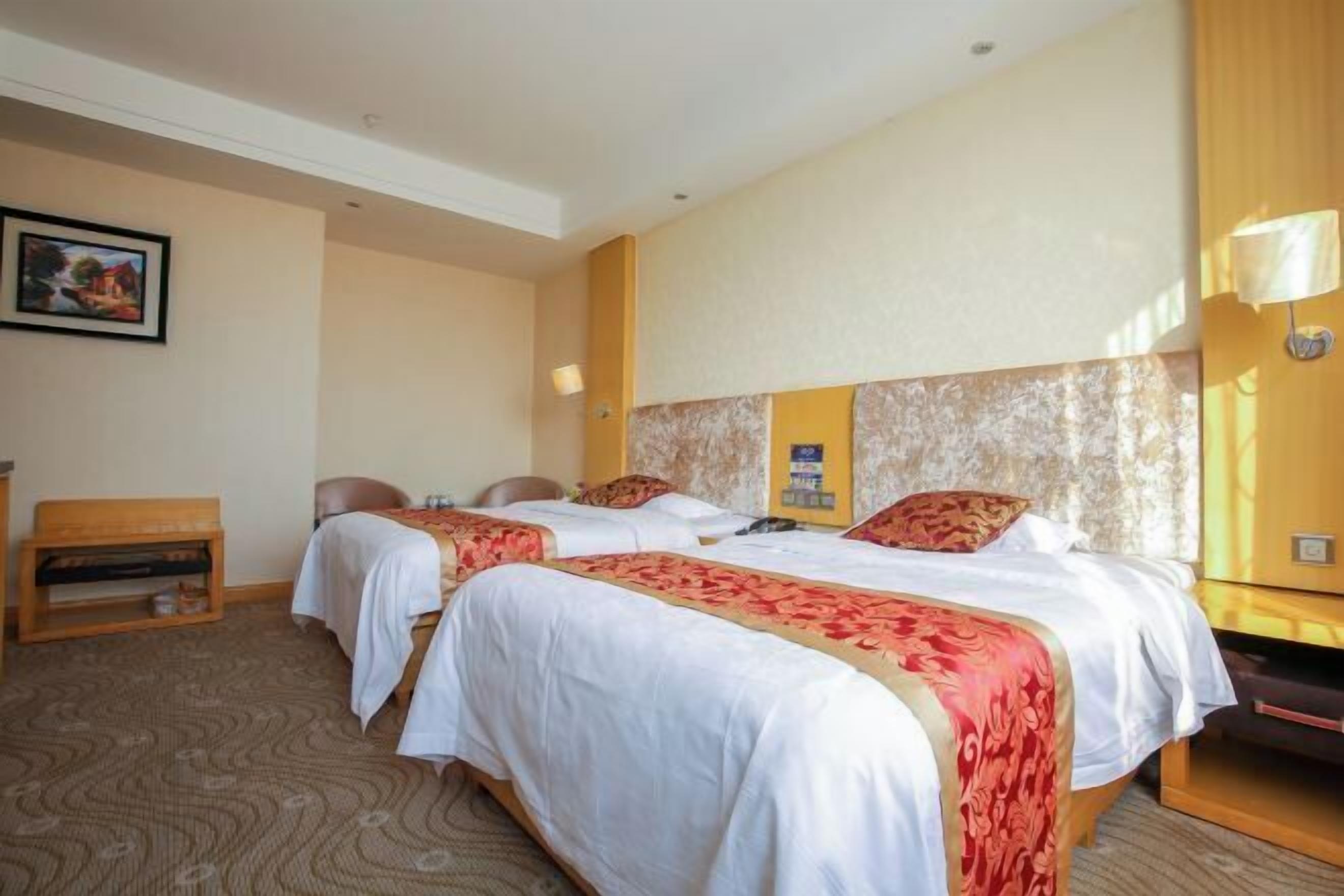 Ein Hotelzimmer mit zwei Betten, einer Holzbank, einem kleinen Tisch und einer Wandlampe.