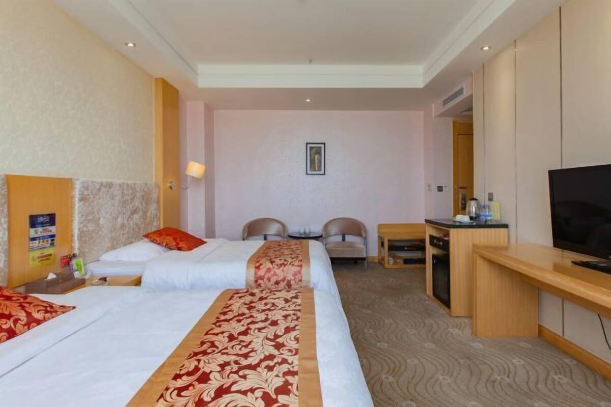 Hotellihuone, jossa on kaksi sänkyä, työpöytä, televisio ja pieni oleskelualue.