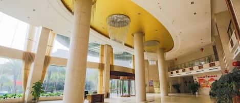 A spacious lobby with high ceilings, large columns, and a central chandelier.
