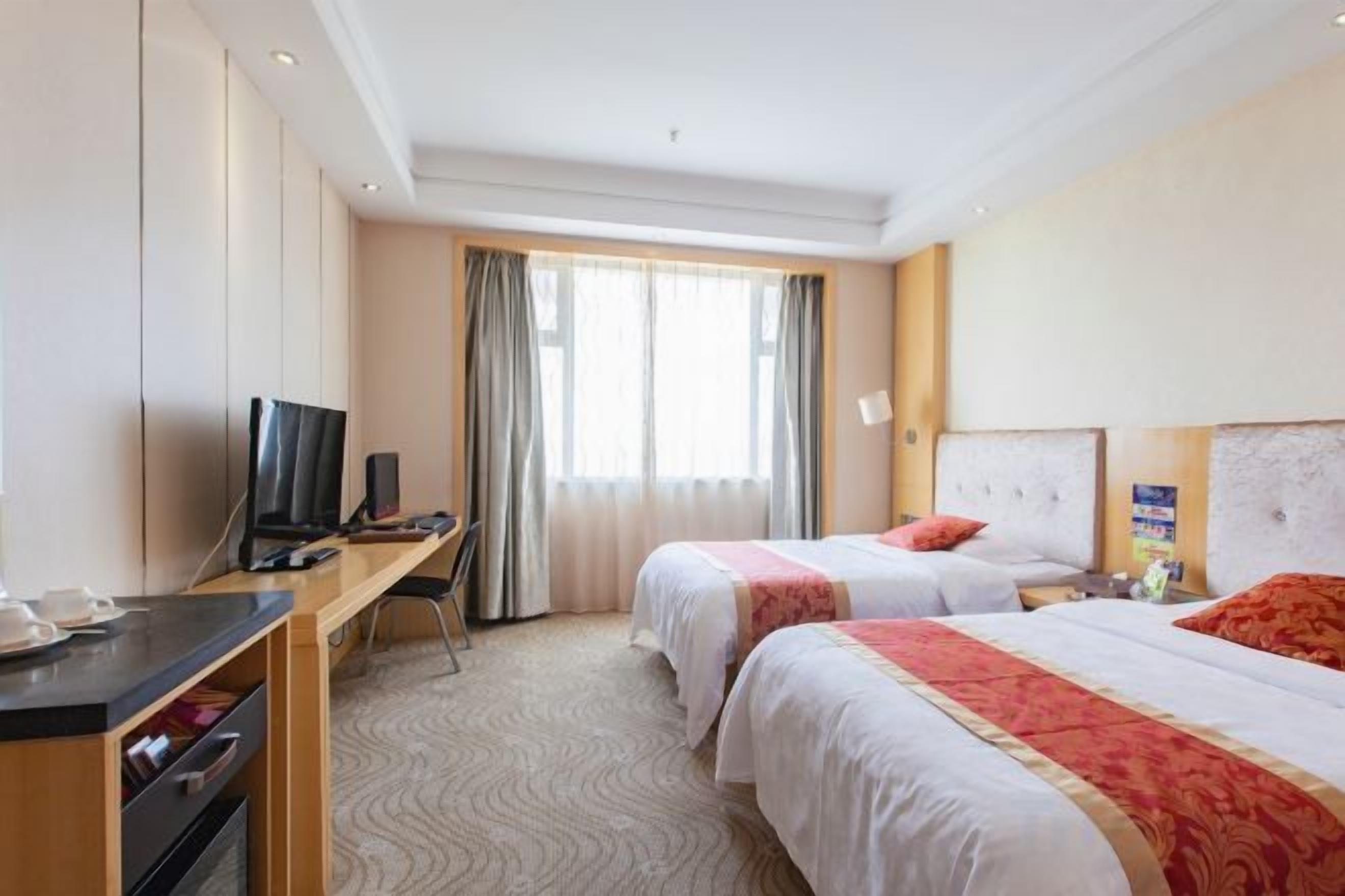 A hotel room with two beds, a desk with a chair, a television, and a window with curtains.