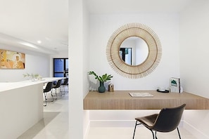 A modern reception area with a wooden counter, a large circular mirror, a potted plant, and a black chair.