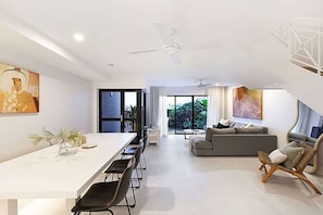 A modern living room with a dining area, a sofa, a chair, and a ceiling fan.