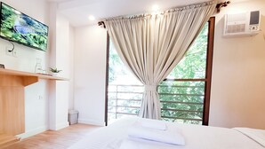 A hotel room with a bed, a TV mounted on the wall, a window with curtains, and a small shelf with items. - Areca Boracay Bed & Breakfast (Boracay Island)