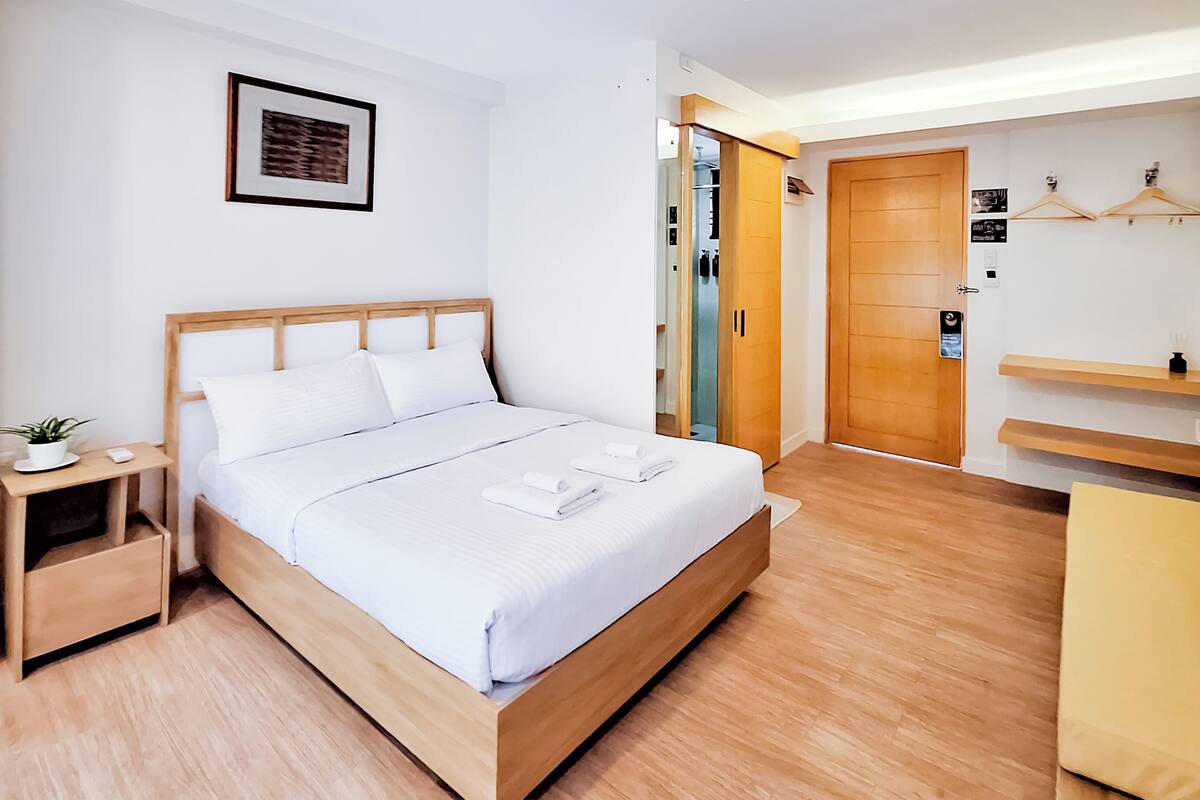 Un dormitorio ordenado con una cama de madera, una mesita de noche con una planta, un armario y un estante pequeño con un gancho.