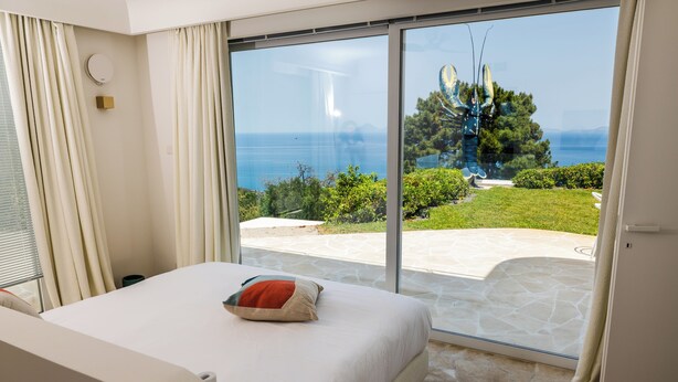 A bedroom with a large sliding glass door leading to a patio with a view of the sea and greenery. - The Sicily Lobster House (naso)