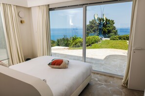 Une chambre dotée d’une grande porte-fenêtre coulissante donnant sur une terrasse avec vue sur la mer et la verdure.