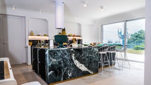 A modern kitchen with a marble island, white cabinetry, and a large window offering a view of the outdoors. - The Sicily Lobster House (naso)