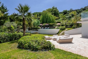 A landscaped outdoor area with a pool, lounge chairs, and a staircase leading to a covered seating area.
