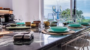 A dining table set with plates, bowls, and wine glasses, with a view of the outdoors through a large window. - The Sicily Lobster House (naso)