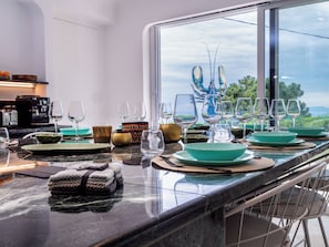 A dining table set with plates, bowls, and wine glasses, with a view of the outdoors through a large window.