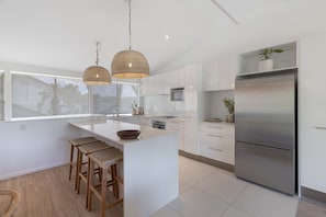 A modern kitchen with a central island, stainless steel appliances, and a large window. - Riverfront Luxury - Poolside, Near Hastings (Noosa)