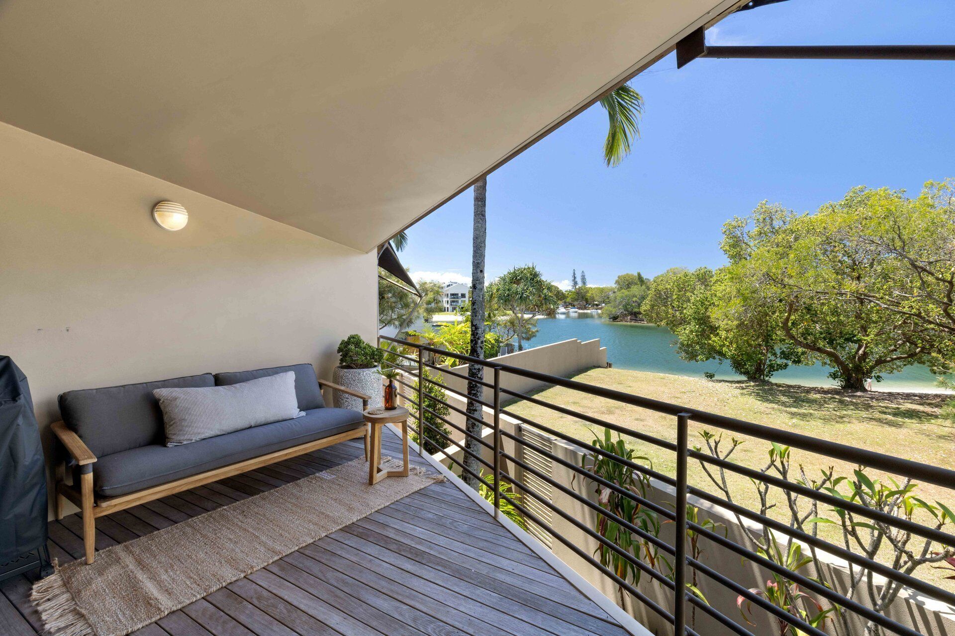 A balcony with a sofa, a small rug, and a view of a lake and trees.