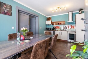 A modern kitchen with a dining area, featuring a long table, chairs, and various appliances.