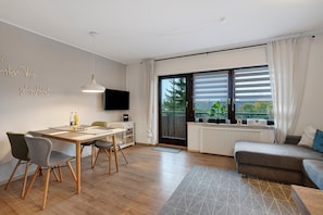 A modern living room with a dining area, a sofa, a TV, and a view through a large window.