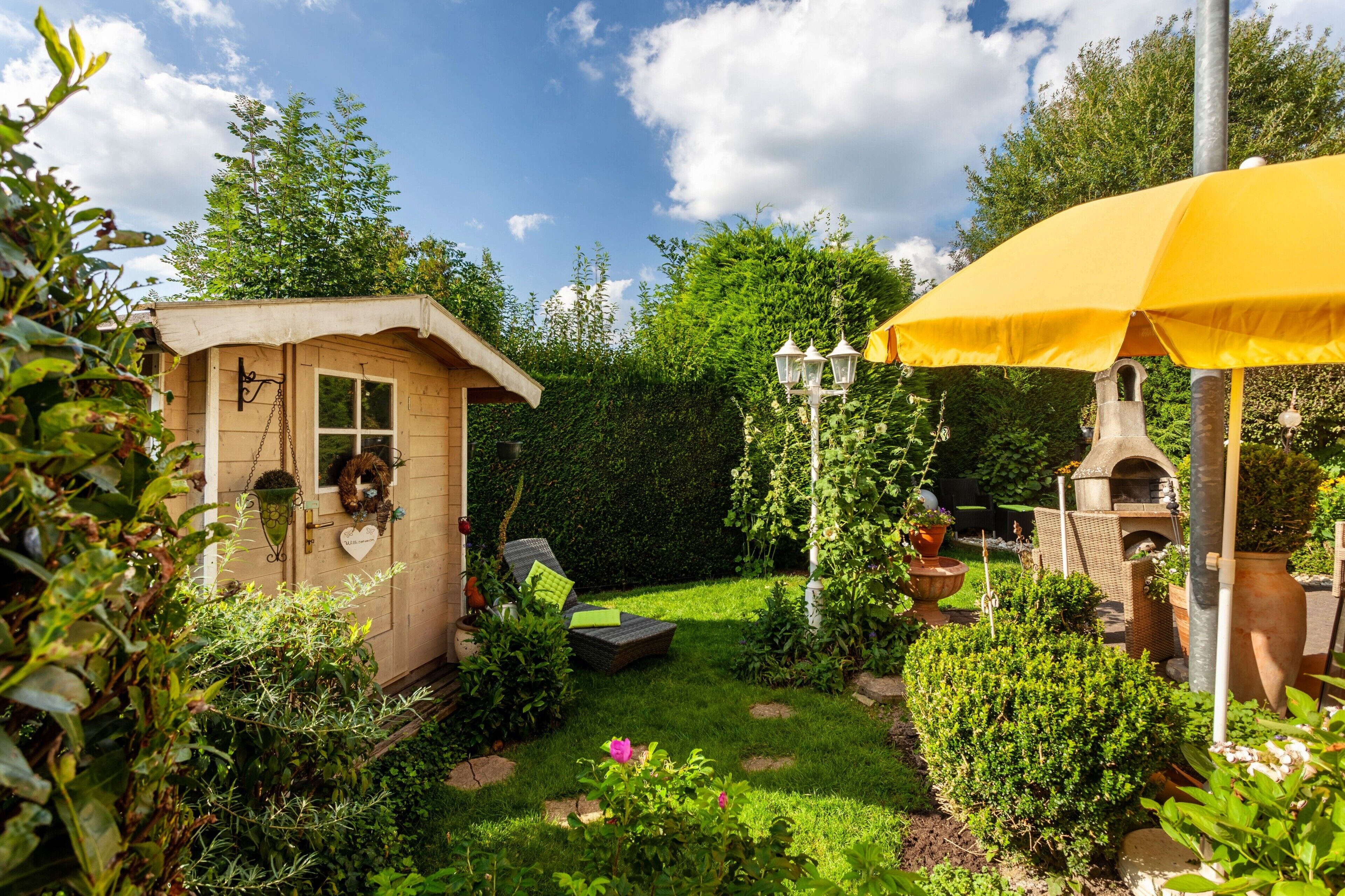 A wooden shed, a yellow umbrella, and a brick oven in a garden.