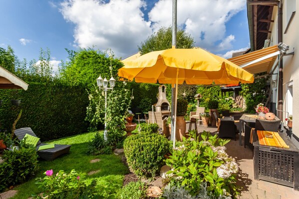 A patio with outdoor furniture, a yellow umbrella, and a garden with various plants and a hedge.