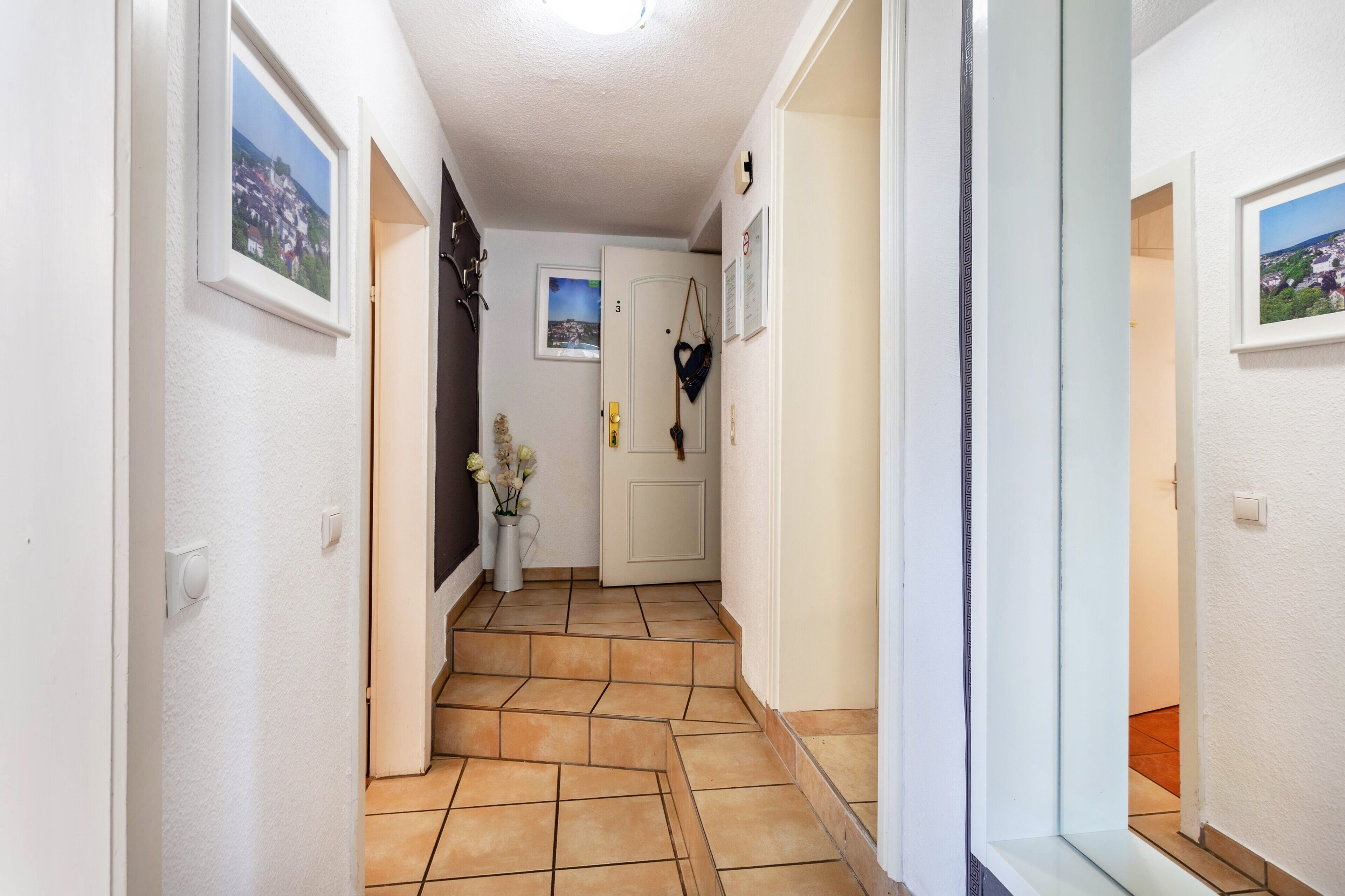 A hallway with tiled flooring, white walls, and framed pictures.