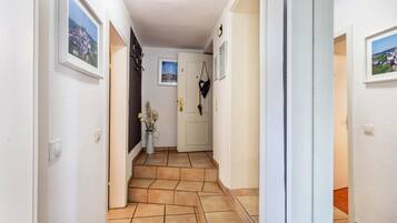 A hallway with tiled flooring, white walls, and framed pictures.
