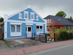 Ein zweigeschossiges Haus mit blauer Fassade, weißem Zierdekor und einem begrenzten Auffahrtsweg.