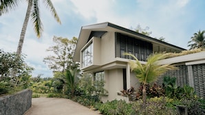A modern house with a paved driveway, surrounded by lush greenery and palm trees. - Sunyi Ubud (Payangan)
