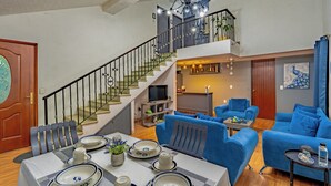 A spacious living area with a dining table set for four, a staircase, a blue sofa, and a television in the background. - Residencia en la ciudad de Oaxaca (Oaxaca de Juárez)