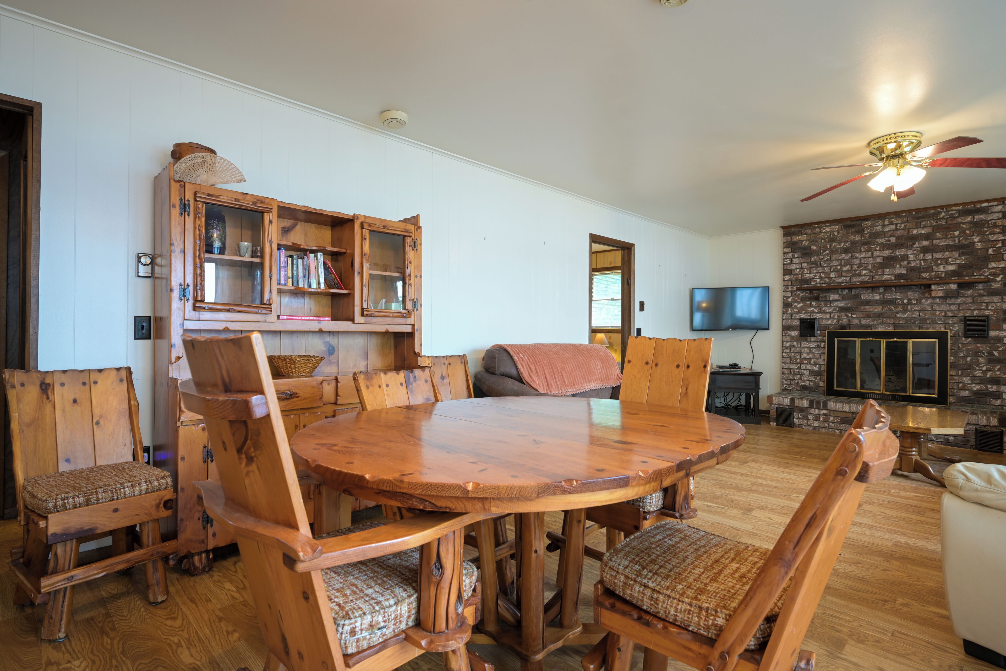 A wooden dining table surrounded by chairs, a bookshelf, a television, and a fireplace.