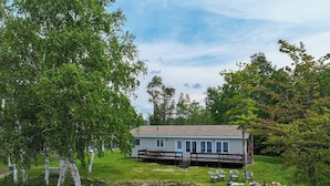 A lakeside cabin with a dock, surrounded by trees and a grassy area. - Rustic, Cozy Lakefront Cabin with Private Beach on Upper Chateaugay Lake. (Lyon Mountain)