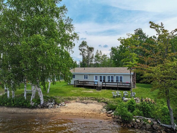 A lakeside cabin with a dock, surrounded by trees and a grassy area.
