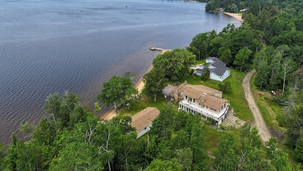 A large house with a spacious porch, surrounded by dense forest and a lake. - Rustic, Cozy Lakefront Cabin with Private Beach on Upper Chateaugay Lake. (Lyon Mountain)
