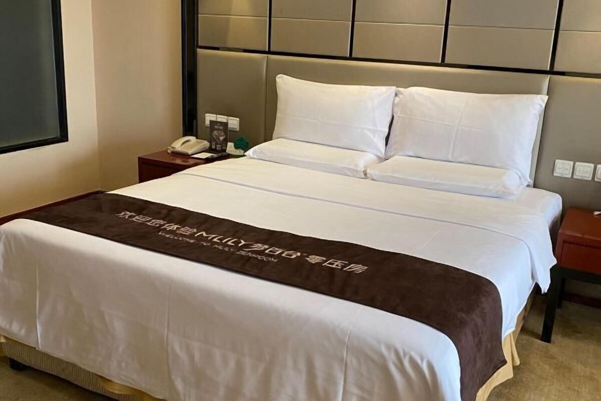 Une chambre d’hôtel avec un grand lit, une table de chevet avec un téléphone et une couverture de lit marron ornée de motifs.