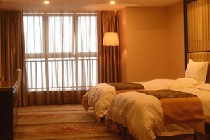 Une chambre d’hôtel avec deux lits, une grande fenêtre avec des rideaux, une lampe et un sol recouvert de moquette.