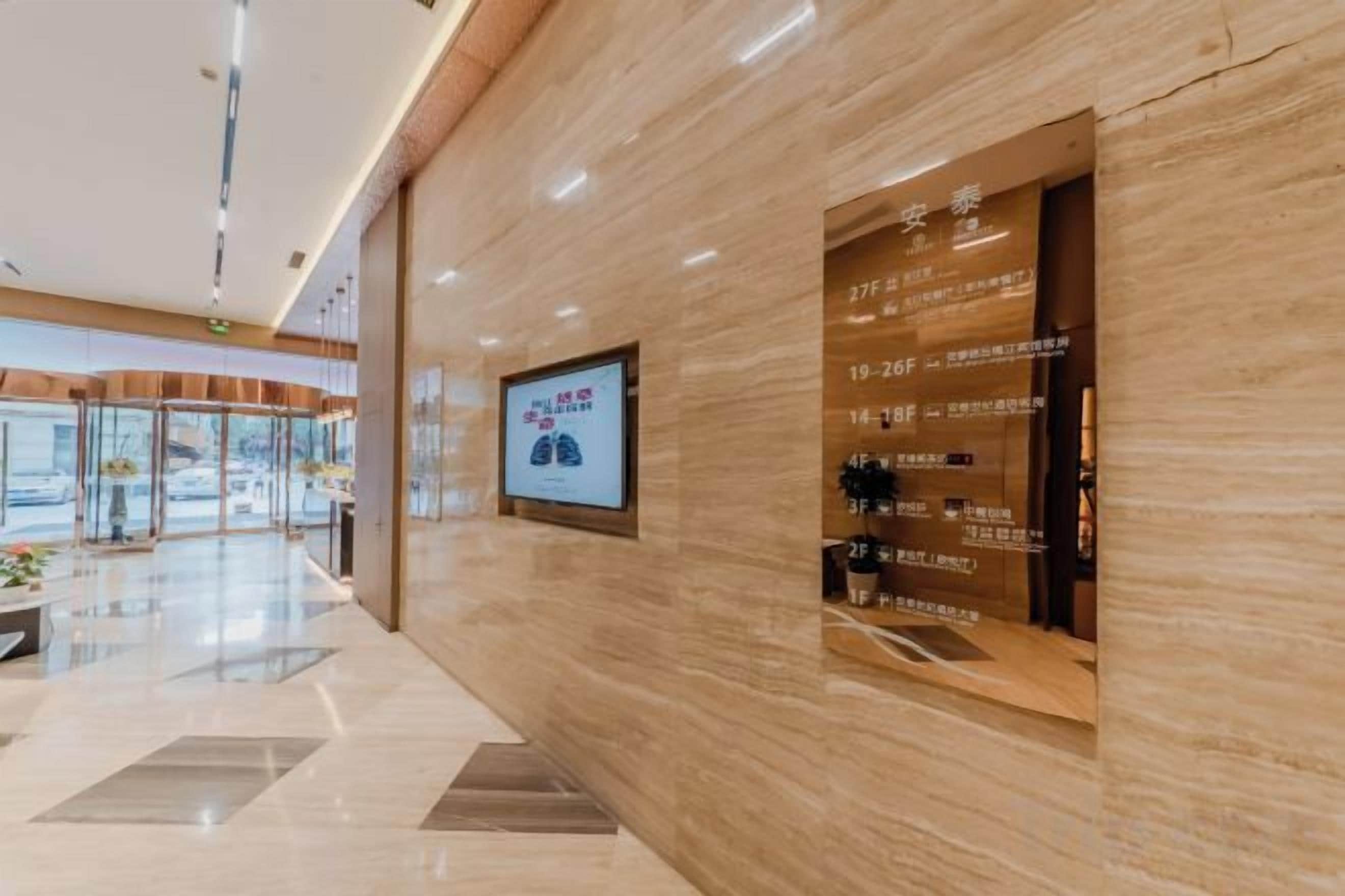 A hotel reception area with a marble wall, a digital screen displaying information, and a directory of rooms.
