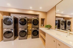 A laundry room with four stacked washing machines and a sink with a mirror above it. - Antai Century Hotel (Chengdu)