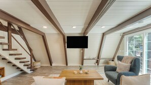 Amplia sala de estar con escalera de madera, televisor de pantalla plana montado en la pared, sofá cómodo y una mesa de centro.
