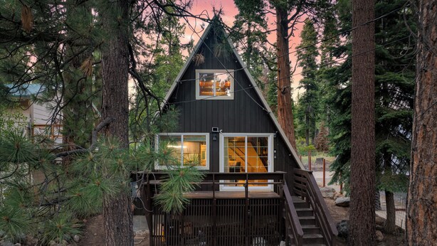 Una cabaña con una terraza de madera, una escalera y un ventanal con vistas a un bosque.