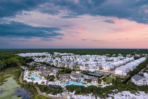 An aerial view of a coastal resort with multiple buildings, a swimming pool, and surrounding greenery. - Shine on the Shore by AvantStay | Pool + Golf Cart (Inlet Beach)