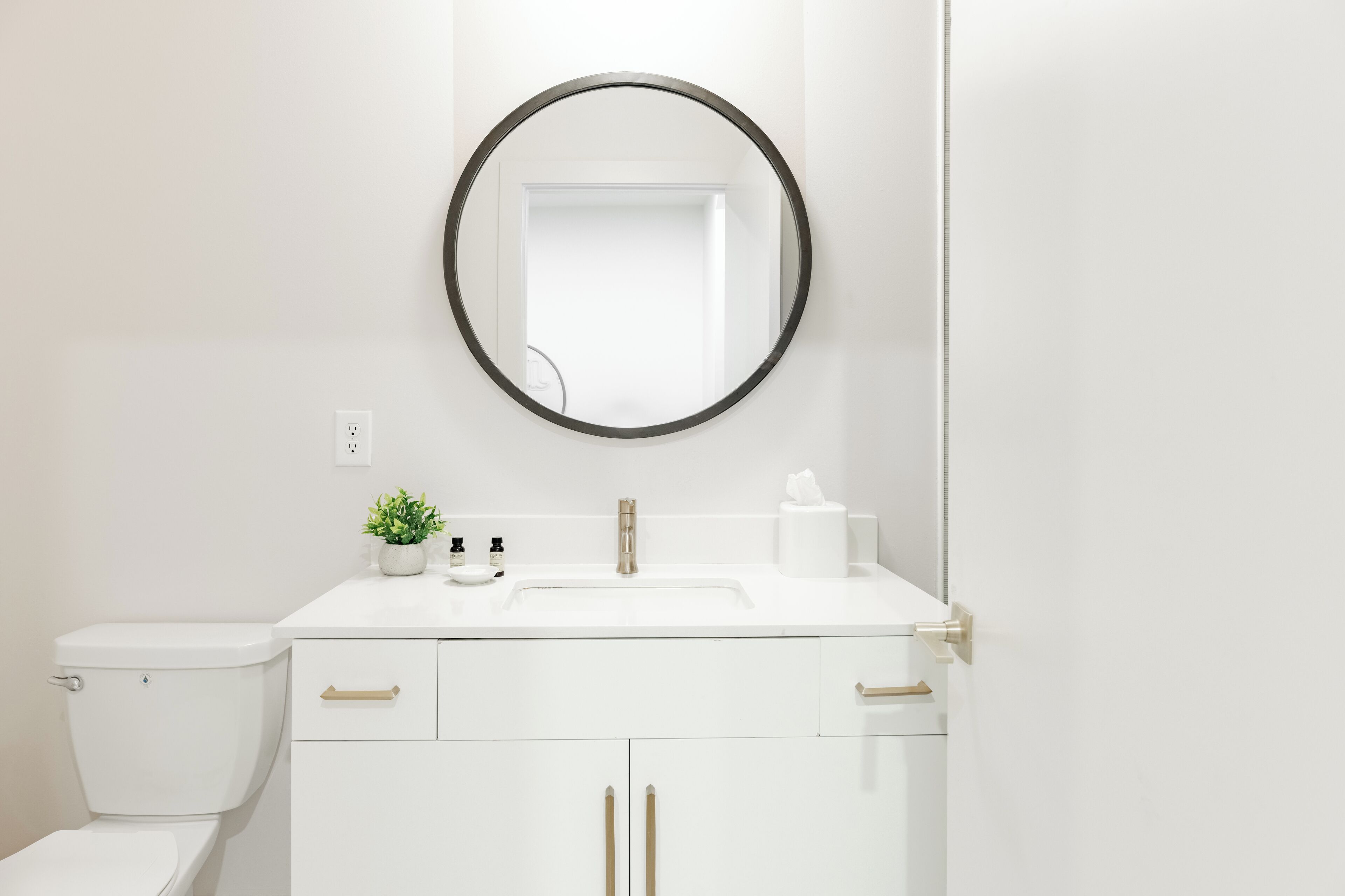 A modern bathroom with a white sink, a round mirror, and a toilet.