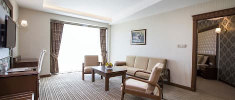 A hotel room with a sofa, two armchairs, a coffee table, a TV, and a large window with curtains.