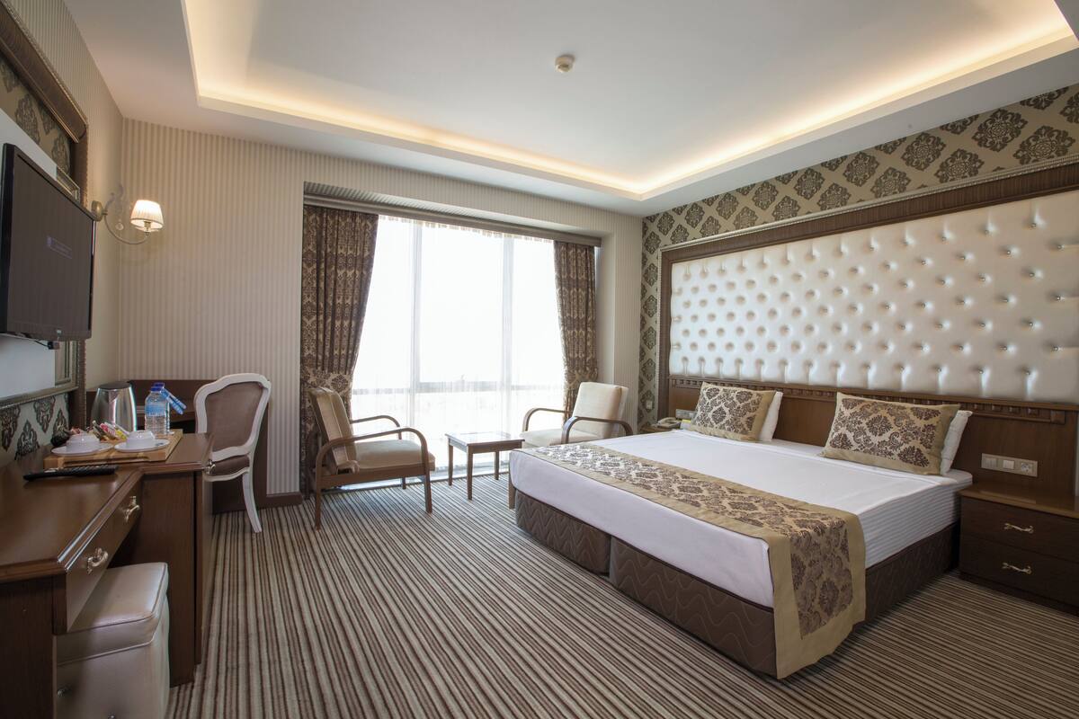 A hotel room with a large bed, two chairs, a desk, a television, and a window with curtains.