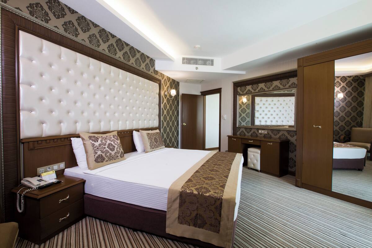 A hotel room with a large bed, a bedside table with a phone, a mirror, and a wardrobe.