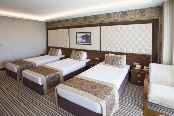 A hotel room with three beds, a large padded headboard, a bedside table with a lamp, and a chair.