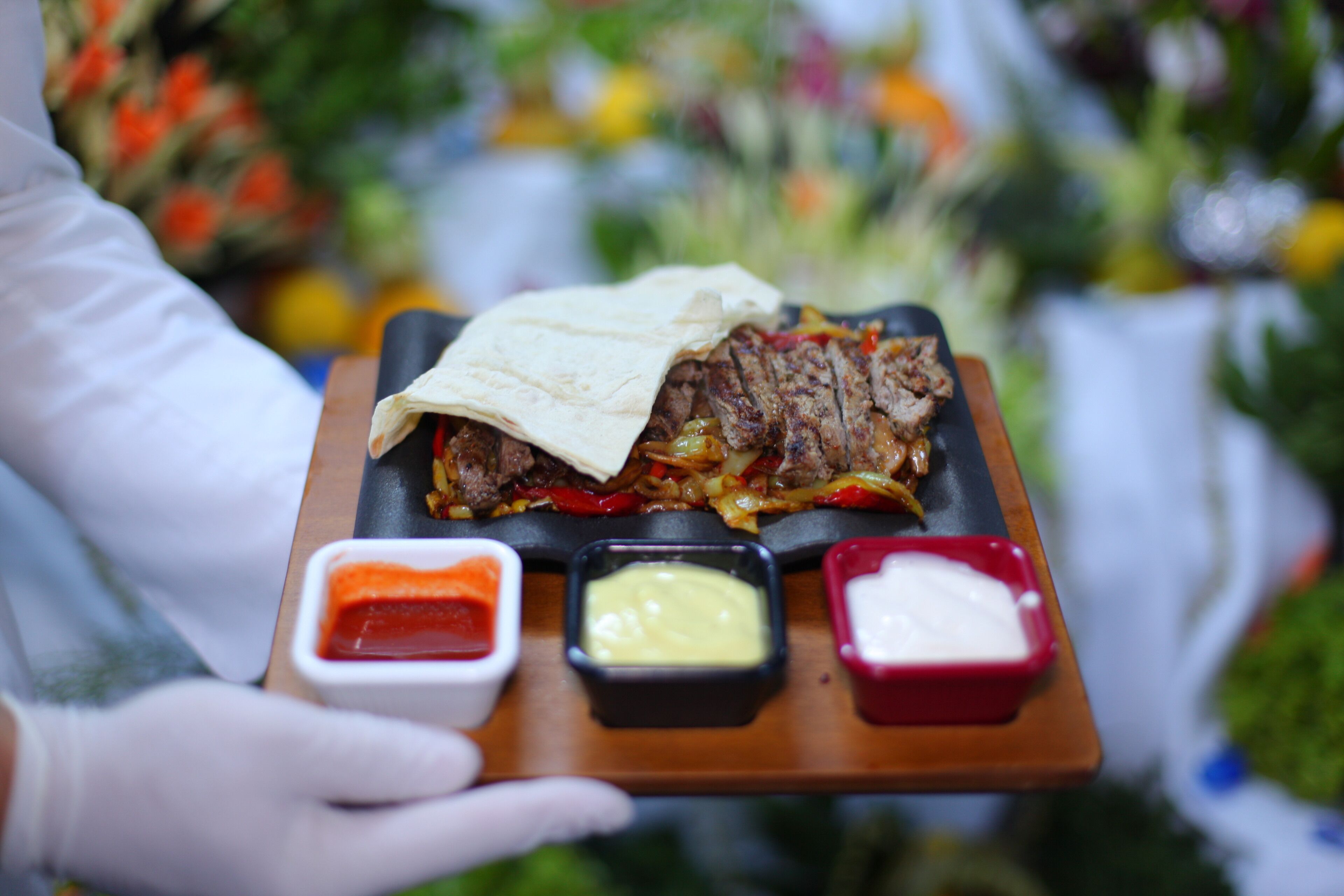A person holding a tray with a meat dish, two sauces, and a folded tortilla.
