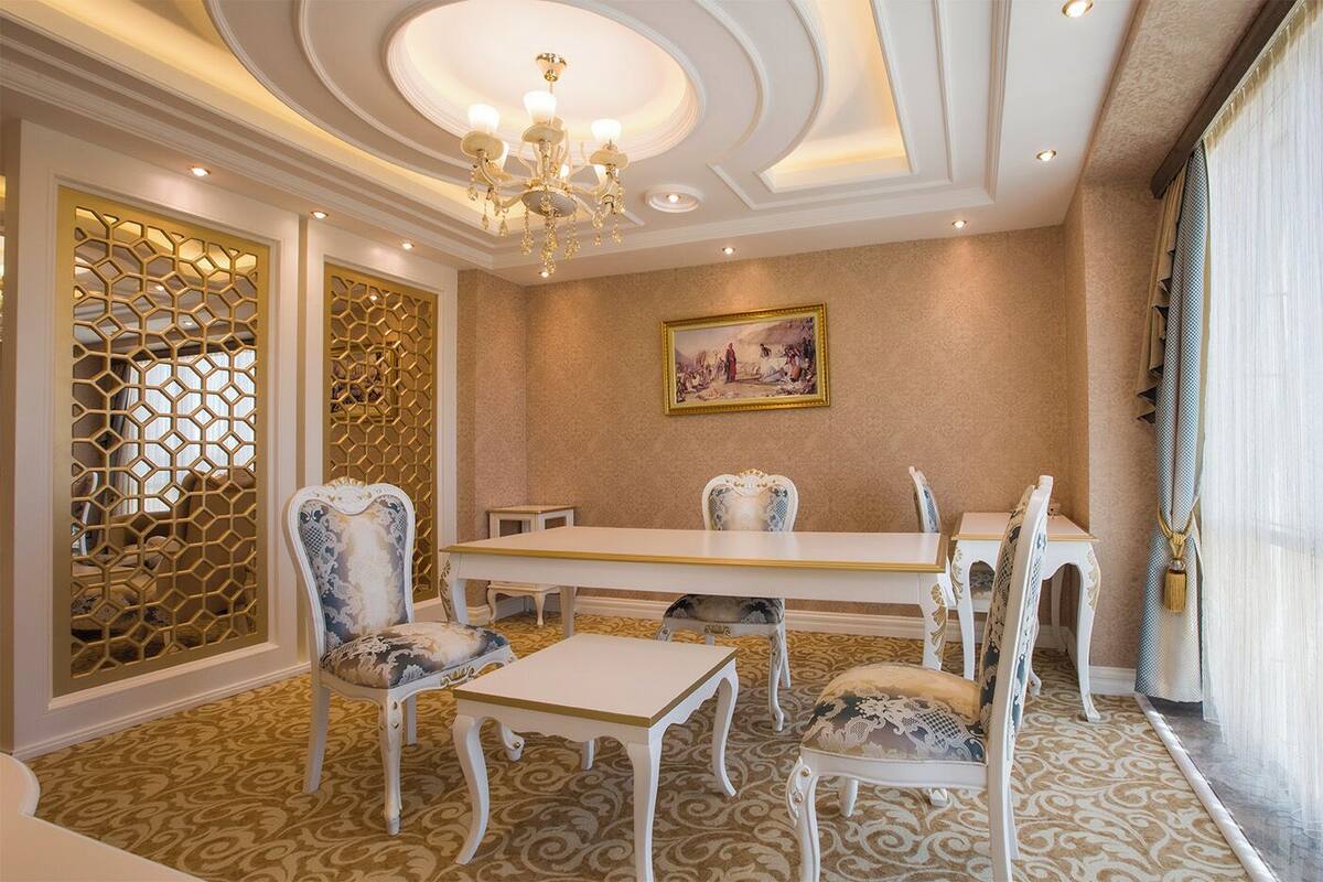 A dining room with a white table and chairs, a chandelier, and a painting on the wall.