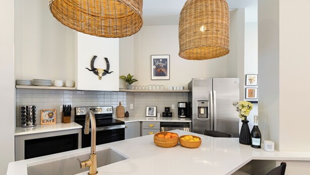 A modern kitchen with white countertops, stainless steel appliances, wicker pendant lights, and decorative items like a bullhorn and framed pictures. - 10 Min to Downtown | The Outrider 4BR Suite (Nashville)